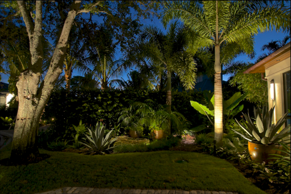 Subtle LED down lighting creates a soft and ambient glow on this property's cobble stone driveway and beautifully contrasts with the dramatic presence of the landscape's lush and tropical vegetation. 