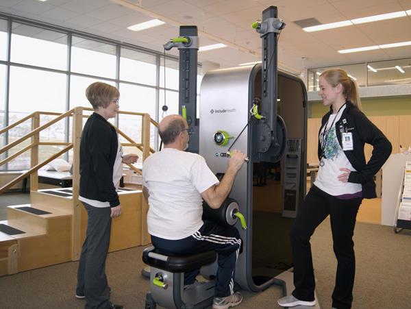 Phil Echert, a patient in the Muscle2Mind pilot program at HealthPartners, exercises with an IncludeHealth and the help of both his exercise physiologist Christa Lence and his caregiver Heather Echert.