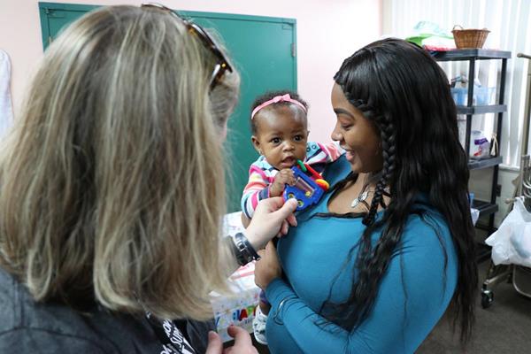Karlita Gulledge (right) holds her daughter, Majesty, as a volunteer at The Luke Project 52 Clinic dotes on her. 